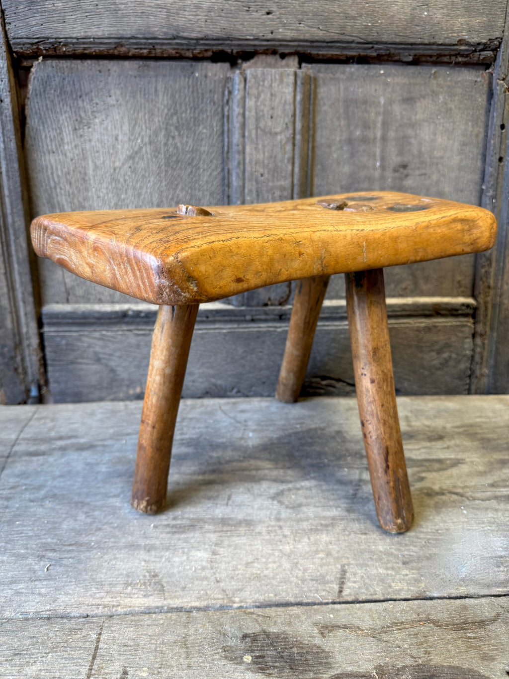 An 18th century elm slab top stool standing over three legs