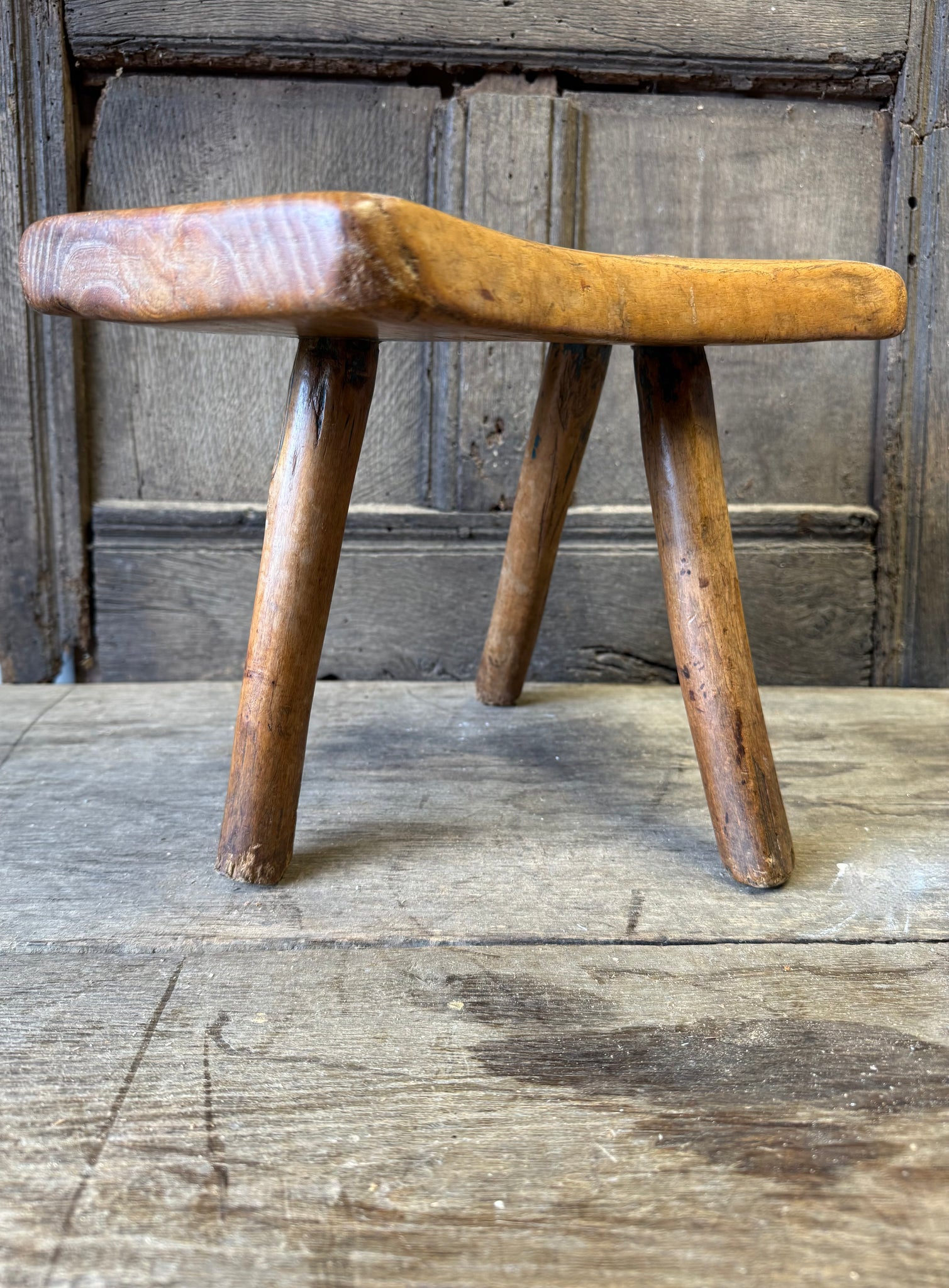 An 18th century elm slab top stool standing over three legs