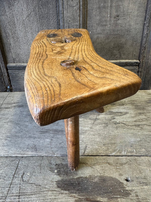 An 18th century elm slab top stool standing over three legs